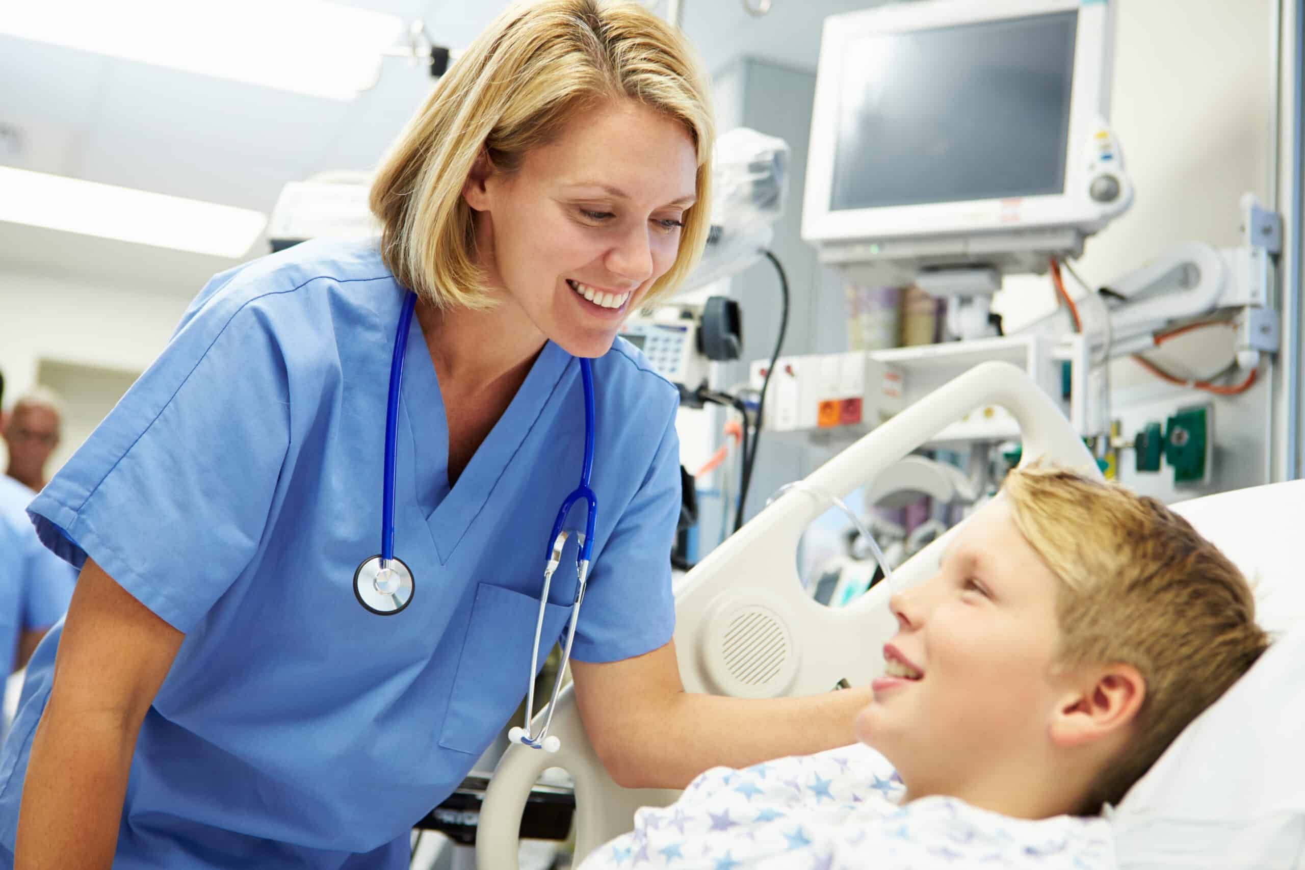 Neurological assessment – a female nurse in blue scrubs speaking with a child boy patient in a hospital bed.